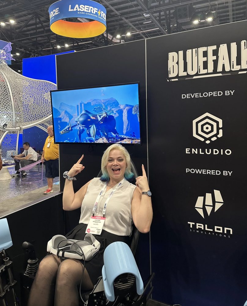 Lilly at the Bluefall booth at IAAPA Expo, giving a thumbs up from a ride seat.